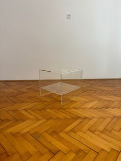 a clear table sitting on top of a wooden floor next to a white wall in an empty room