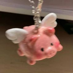 a pink piggy keychain hanging from a chain with angel wings on it