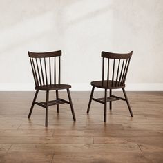 two wooden chairs sitting side by side on a hard wood floor in front of a white wall