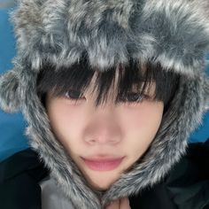 a young man wearing a furry hat with fur on it's hood and his hands under his chin