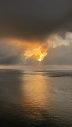 the sun is setting over the ocean with dark clouds in the sky and water below