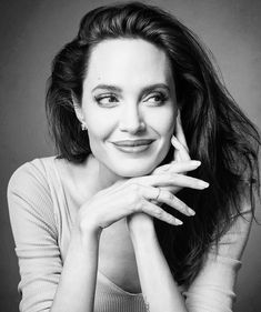 a black and white photo of a woman with her hands on her chin, smiling