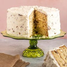 a cake with white frosting is on a green platter next to a piece of cake