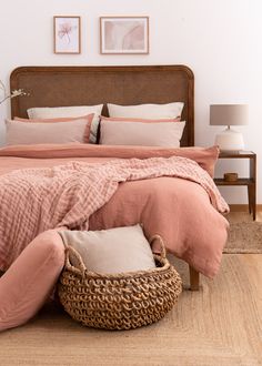 a bed with pink linens and pillows in a white room next to a wicker basket