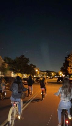 several people riding bikes down the street at night with their lights on and one person walking behind them