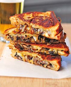 two grilled sandwiches stacked on top of each other next to a glass of beer