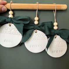 three white ceramic ornaments hanging from a wooden hanger with green ribbon and wood bead