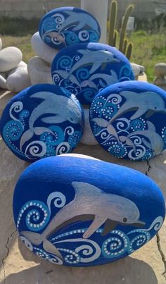 three painted rocks with dolphins on them