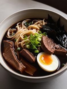 a bowl of ramen with meat, noodles and an egg in it on a table