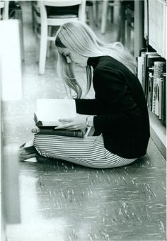 a woman is sitting on the floor writing in her notebook and looking down at books