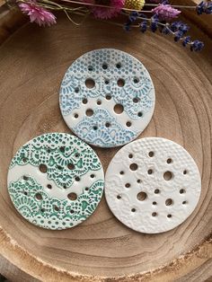 three white and blue buttons sitting on top of a piece of wood with flowers in the background