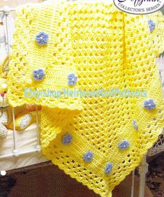 a crocheted yellow blanket with blue flowers on it and a teddy bear next to it