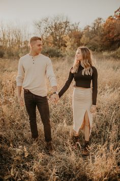 an engaged couple holding hands and walking through tall grass