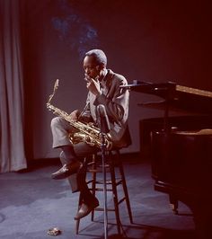 a man sitting in front of a piano playing a saxophone on top of a stool