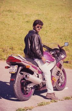 a man sitting on the back of a motorcycle next to a grassy field and road