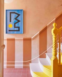 a painting hangs on the wall next to a stair case in a pink and yellow room