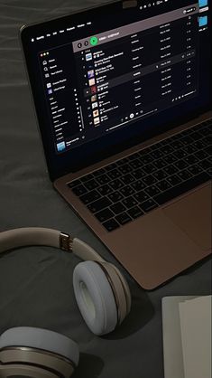 an open laptop computer sitting on top of a table next to headphones and a book