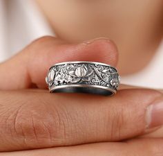 a close up of a person's hand holding a silver ring with flowers on it