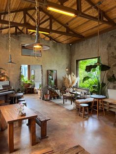 a large open room with wooden tables and benches in front of a window that looks out onto the jungle