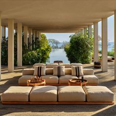 an outdoor living area with couches and tables on the ground next to some water