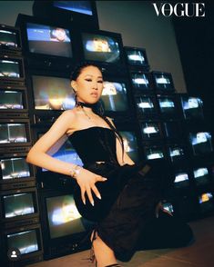 a woman in a black dress is posing for a photo with televisions behind her