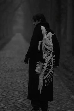 a person walking down a road with a skeleton on it's back, in the dark