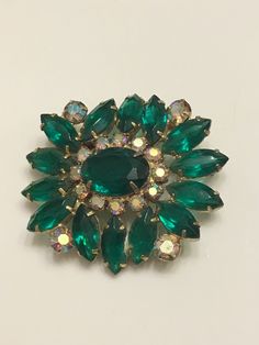 Vintage green glass cabochon and marquise rhinestone brooch no hallmark. Circa 1950's. There are 2 different colored rhinestones and 3 different shapes. The stones are complete and pronged together securely. Beautiful floral design with borealis stones on the corners. This will be an addition to a beautiful rhinestone brooch collection. Green Oval Brooches For Formal Occasions, Mid-century Green Brooch For Formal Occasions, Mid-century Green Brooches For Formal Occasions, Green Mid-century Style Brooches For Formal Occasions, Mid-century Green Formal Brooches, Retro Green Brooch Jewelry, Retro Green Jewelry For Vintage Events, Antique Green Brooch For Evening, Vintage Green Brooch For Evening