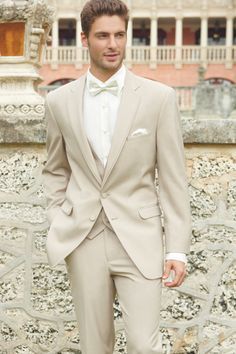 a young man in a tuxedo standing on the grass with his hands in his pockets