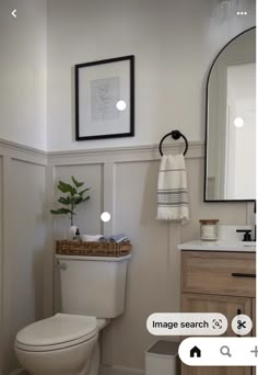 a white toilet sitting in a bathroom next to a sink under a framed picture on the wall