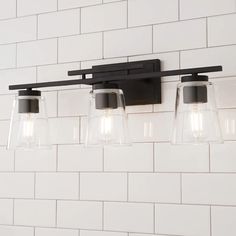 a bathroom light with three lights on the wall and white brick walls behind it,