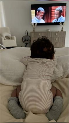 a baby laying on top of a bed in front of a tv