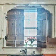 a kitchen sink sitting under a window with shutters on the windowsill and flowers in a vase