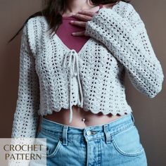 a woman wearing a white crochet sweater and blue jeans with her hands on her chest