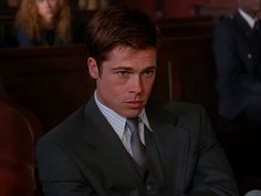 a man in a suit and tie sitting at a table with other people behind him