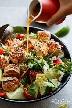 someone pouring dressing onto a salad with meatballs and veggies in a bowl