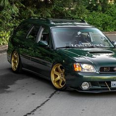 a green car with gold rims parked on the street in front of another car