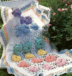 a crocheted blanket sitting on top of a grass covered ground next to flowers