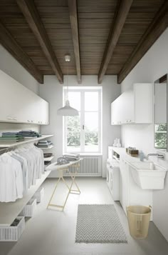 a white laundry room with lots of clothes hanging on the rack and shelves next to it