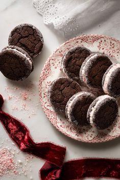 chocolate cookies with powdered sugar on a plate next to a red ribbon and white doily