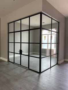 an empty room with glass walls and wood flooring in front of the door to another room