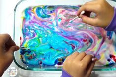 two children are painting the inside of a glass container with colorful fluid paint on it