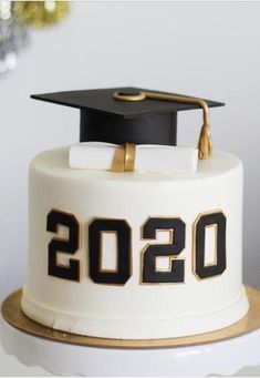 a white cake with black and gold decorations on it, decorated with a graduation cap