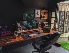 a desk with speakers, laptop and other items on it in front of a window