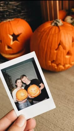 a person holding two pumpkins in front of some jack - o'- lanterns