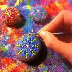 someone is painting rocks with colored paint on them and using a pen to draw the designs