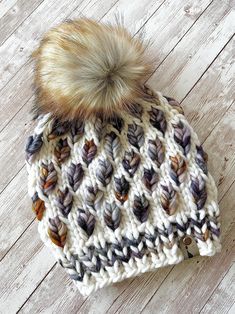 a white and brown knitted hat with a fur pom on top sitting on a wooden floor