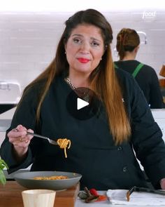 a woman holding a spoon and fork in front of a bowl filled with food on top of a table