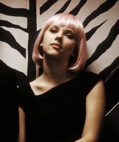 a woman with pink hair sitting next to a zebra print wall