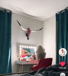 a woman sitting in a red chair next to a window with birds on the wall