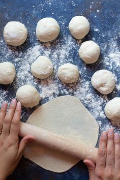 hands rolling dough on a blue surface with floured balls in the foreground and wooden rolling board to the side